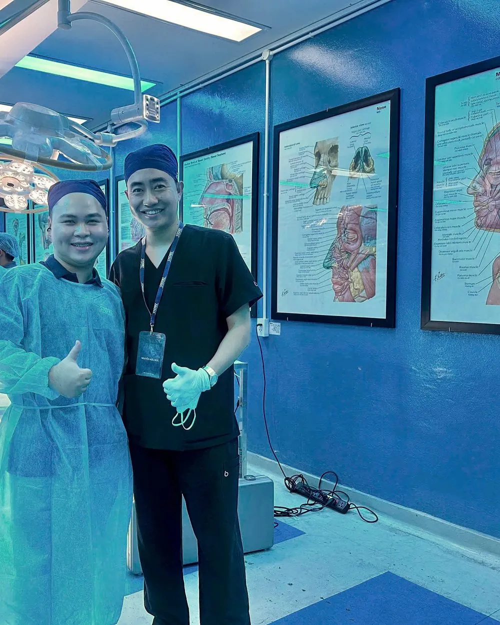 Bác sĩ Đức cùng đồng nghiệp tại phòng thực hành của hội thảo, tường treo tranh giải phẫu vùng mũi và mặt